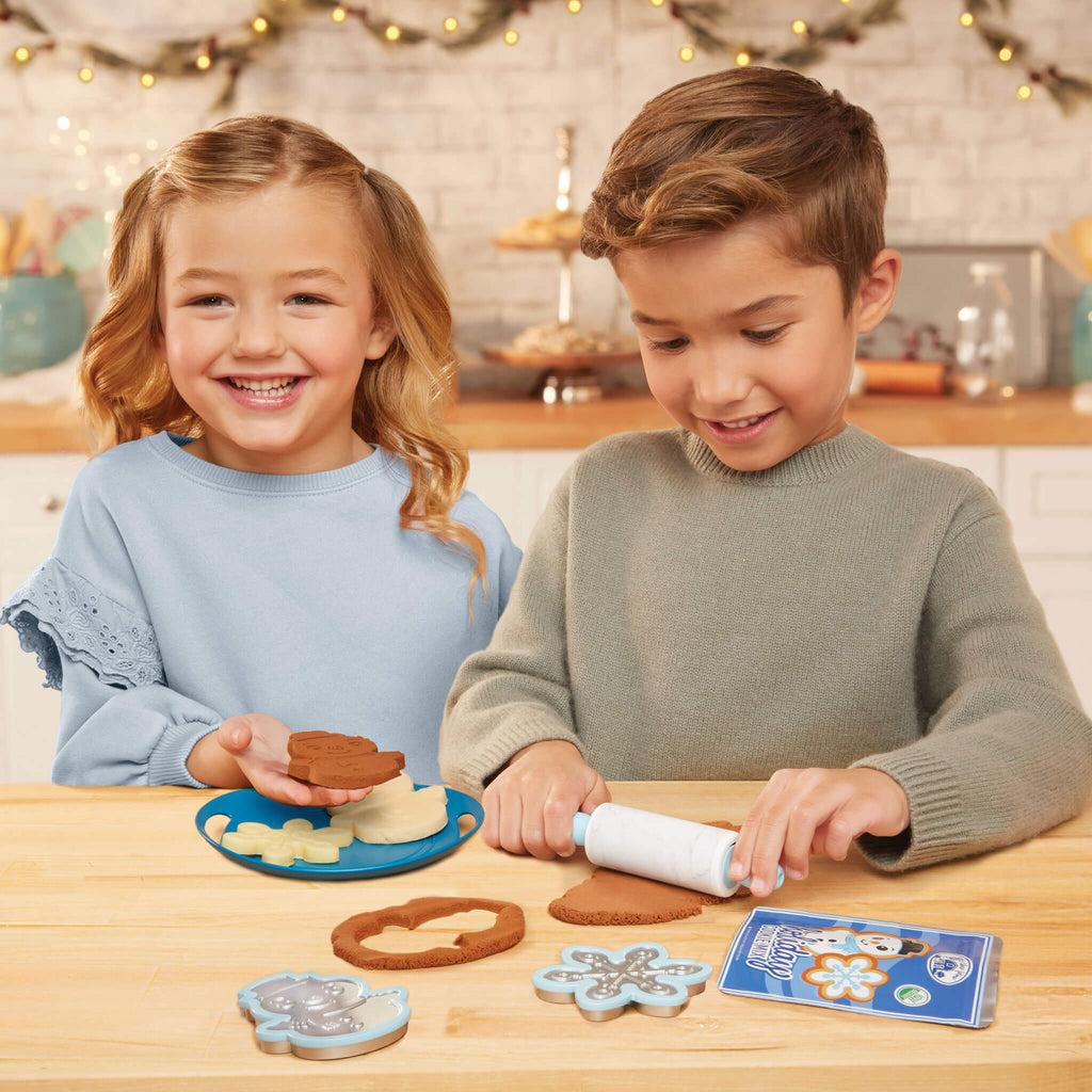 Two children playing with cookie cutters and dough on a wooden table.