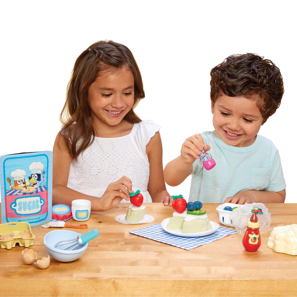Two children playing with Pavlova and utensils on a wooden table.